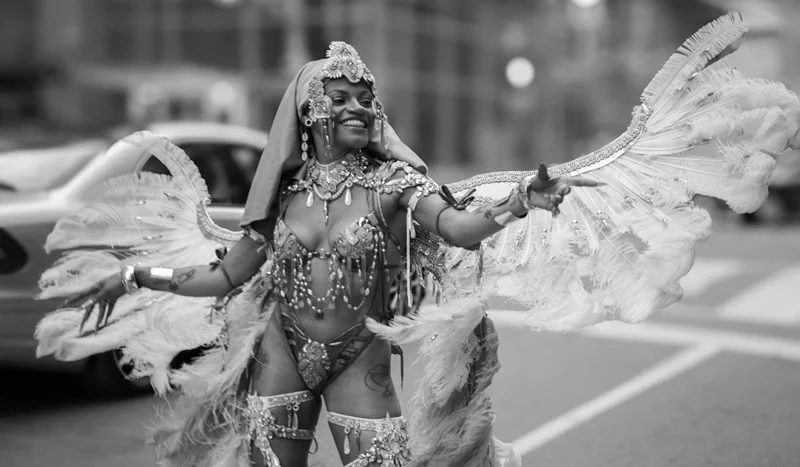 Caribbean Carnival masquerader in an elaborate white feathered costume dancing in the street