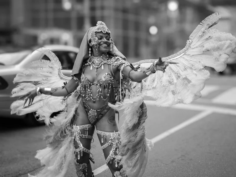 Caribbean Carnival masquerader in an elaborate white feathered costume dancing in the street