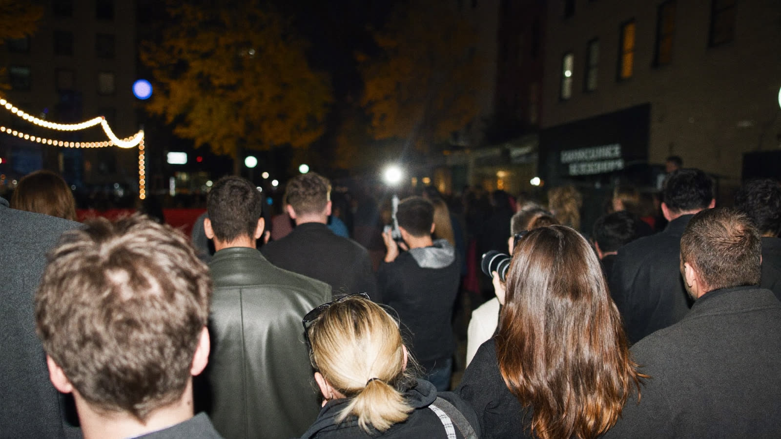 A festival crowd and photographers gathered outside a premiere at night under string lights