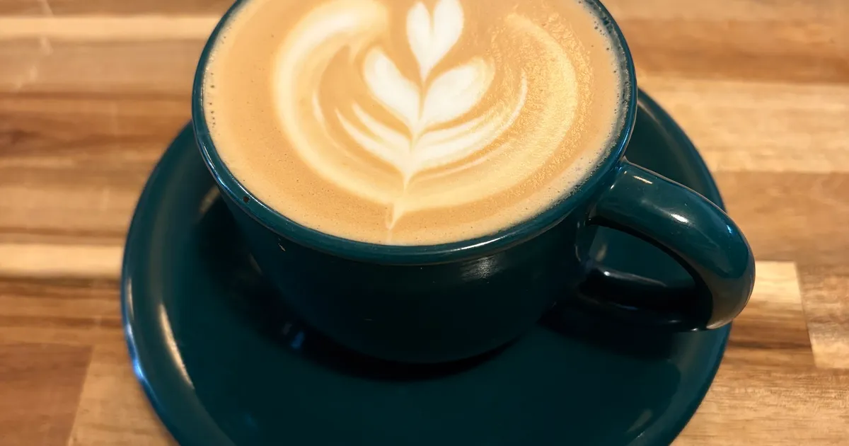 Latte with rosetta art in a teal cup on a wooden table
