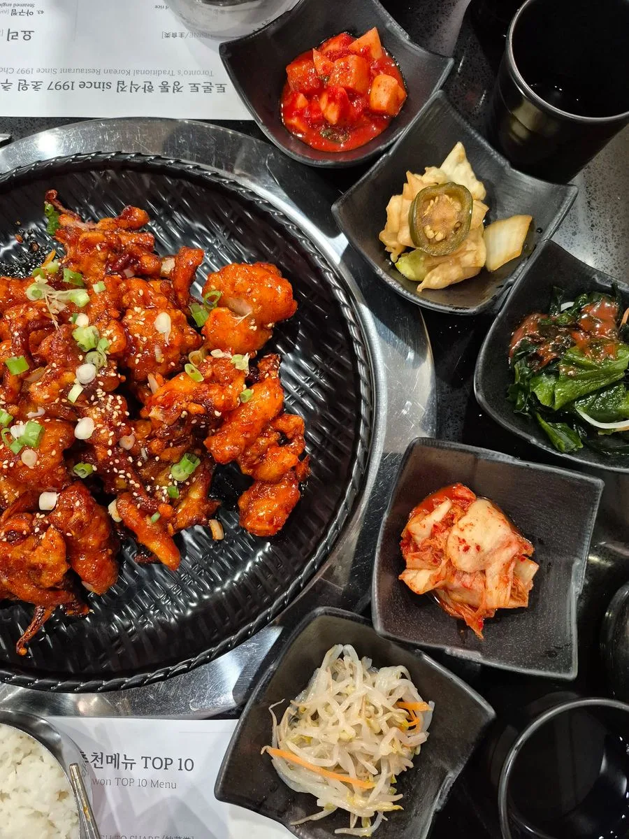 Chowon Korean BBQ spicy chicken with banchan side dishes on a grill table in North York